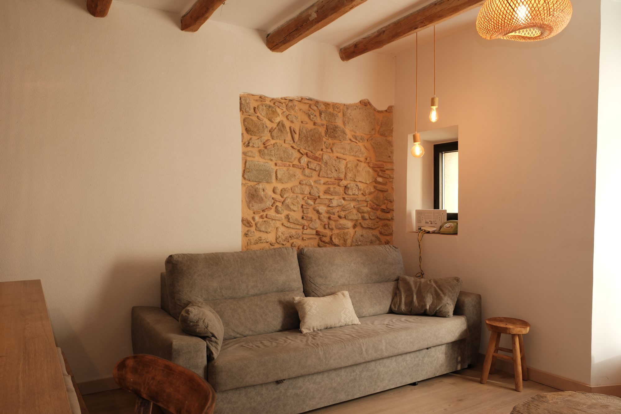 Sala d'estar de Can Joan Empordà amb bigues de fusta i mur de pedra original